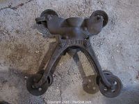 Rusty cast iron triple-wheel barn pulley with 'HERO' cast into body, shown from an angle on a rough surface.