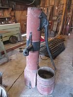 Vintage cast iron water pump with attached spout and handle on a red wooden post, visible wear and age marks.