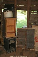 Wide view showing wooden tray and two small shelves stacked and positioned next to each other inside rustic wooden shed.