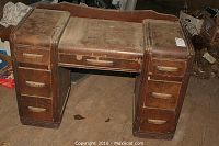 Front view of heavily worn antique wooden desk showing surface wear and drawer arrangement, with all drawers closed.
