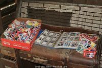Box of loose baseball cards and binder with cards visible on a bench