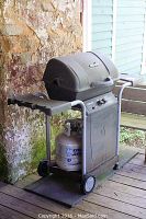 Photo of a Char-Broil gas grill with attached propane tank, black body, side shelf and wheels.