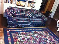 Plaid fabric sofa with matching cushions and area rug underneath in a living space.