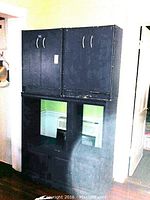 Front view of three-piece black storage cabinet with two upper and one lower cabinet showing visible exterior wear.