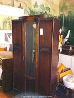 Wooden wardrobe with three doors, center door featuring full-length mirror, dark wood with carved side panels.