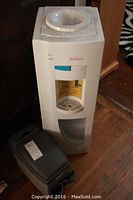 Photo showing the white Sunbeam water dispenser with the black car console cooler placed next to it on the floor.