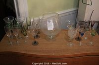 Wide view of wine glass collection including colorful and etched glasses along with large decorative wine glass vase on wooden surface.
