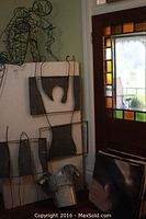 Overall view of white display block leaning against wall with three metal sculptures attached and others propped around it in front of stained glass window