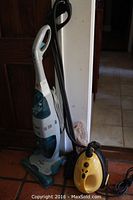 Photo showing Hoover Floor Mate H300 hard floor cleaner with white and teal body, standing next to yellow Lil Steamer 2 steam cleaner with black hose and cords.