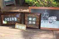 Five framed artworks arranged outdoors on wooden surface: framed Parsin print, two floral vertical frames, one 18x30 still life scene frame, one 22x22 ornate frame with black and white artwork.