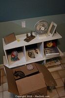 Two white shelves stacked showing boxes of books and various decorations on shelves like photo frames and small figurines.