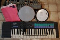 Photo showing Casio CA 100 keyboard, Pearl drum practice head, tambourine, xylophone, and sheet music.