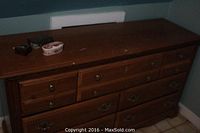 Front view of medium brown wood dresser with seven drawers and brass handles. Top shows wear and scratches. Three small jewelry boxes placed on top left.