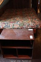 Futon mattress with colorful travel sign pattern and wood shelf unit in front, showing top and storage compartments.