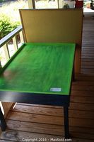 Side and angled view of green wooden activity table with black legs, and a large rectangular wooden craft board behind it.
