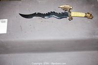 Full view of the decorative knife showing the entire wavy-edged blade and brass dragon handle with textured grip.