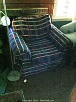 Plaid armchair with cushioned seat and backrest near window and floor lamp base visible beside it.