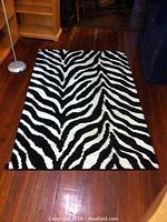Zebra stripe rug shown laid out flat on wooden floor with floor lamp visible in the background.