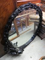 Full view of round ornate black lacquer framed mirror leaning against wood furniture showing overall condition and size.