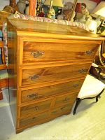 Front view showing the full dresser with six drawers, medium brown wood veneer finish, metal handles, and some surface wear.