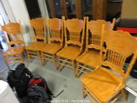 Six wooden dining chairs lined up with carved backs and vertical spindle support below backs.