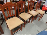 Four wooden dining chairs with beige upholstered seats arranged in a row, showing overall condition and design.