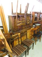 View of four wooden dining chairs stacked on a wooden cabinet, showing the backrest and legs. Visible marks and wear on wood.