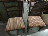 Front view of two wooden chairs with striped upholstered seats, showing ladder back design and wear.
