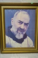 Framed portrait print of a religious figure (Padre Pio) with gold frame showing scratches.