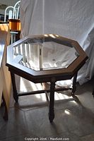 Octagonal glass top end table with wood veneer legs and frame, surface visible from a side angle.