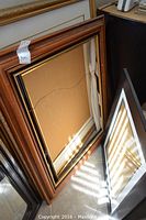 Six frames stacked on floor showing backs and edges, showcasing different frame styles and sizes.