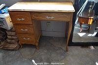 Front view of wood desk on tile floor with three left drawers and one center drawer, showing condition and design