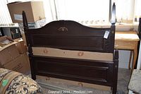Full view of dark wood queen headboard and footboard leaning against a wall with cardboard support between panels.