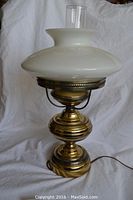 Front view of the vintage brass table lamp showing the white glass shade and clear chimney, brass base details, and power cord