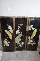 Three black lacquered Asian panels arranged side by side with peacock and flower designs, showing wear and scratches.