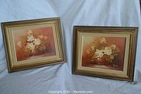 Both framed oil paintings side by side showing white flowers in vases on warm backgrounds, signed 'Aras'