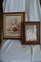 Two framed artworks displayed together, showing oil painting of flowers and a print of a figure with lamb.