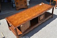Full angled view of wood veneer coffee table showing scalloped edges, wood grain top, cabinet and lower shelving.