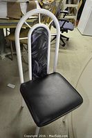 Front view of chair showing white metal tubular frame, black vinyl seat and patterned backrest