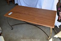 View of rectangular faux wood coffee table top with scratches and chip along edge, showing wood grain finish and metal curved legs underneath.