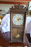 Front view of the Sun Lights wooden pendulum wall clock showing clock face, gold decorative corners, pendulum behind glass, and carved wooden detailing.