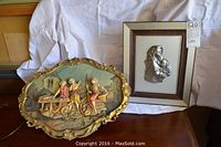 Two wall decor items displayed on wood surface: one framed Peltro Cesellato relief plaque and one gold-framed relief scene of children at table.