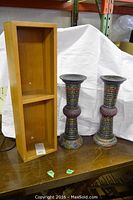 Two decorative candle holders and wood veneer shelf displayed on a table with white backdrop.