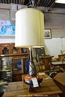 Full view of the vintage lamp showing ceramic base and beige fabric shade on top.