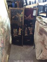 Three Asian decorative panels leaning against a wall, detailed hand-painted scenes visible