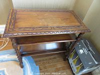 Full view of the occasional table from a corner showing twisted spindle legs, two lower shelves, and the carved walnut finish top with wear marks.