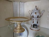 Overview of gilt porcelain pedestal bowl alongside porcelain tea warmer with teapot