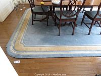 Light blue rug with beige and cream concentric border under dining table
