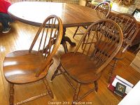 Front view of multiple oak hoop back dining chairs around a dining table on wooden floor.