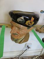 Side view of the ceramic Toby pitcher showing the detailed face of a man wearing a black hat with gold and white decorations.